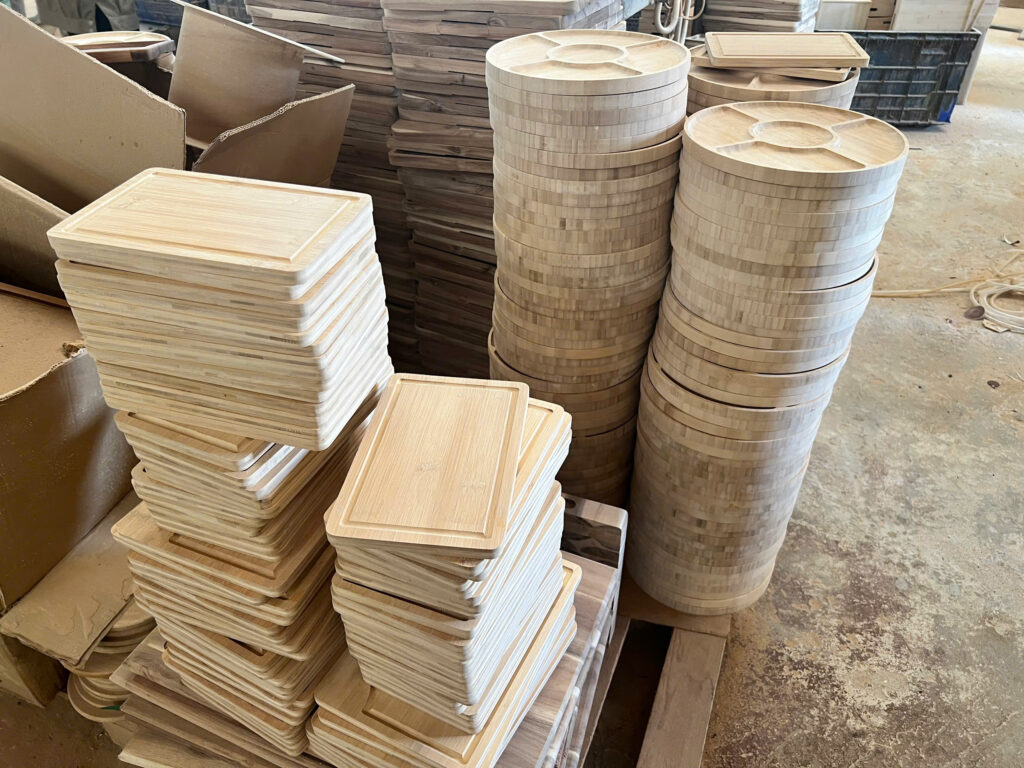 Stacks of finished bamboo cutting boards and round sectioned platters on the factory floor.