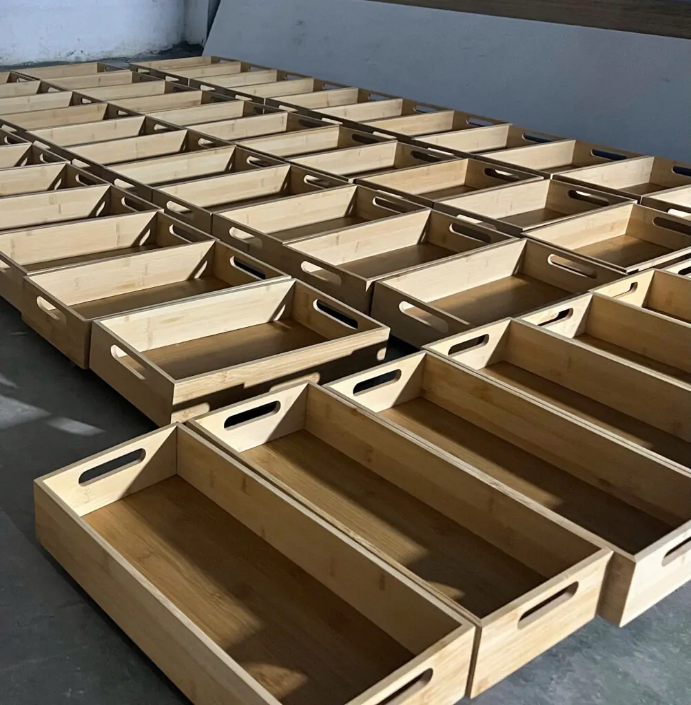 Rows of finished bamboo serving trays with cut-out handles, laid out before packing.